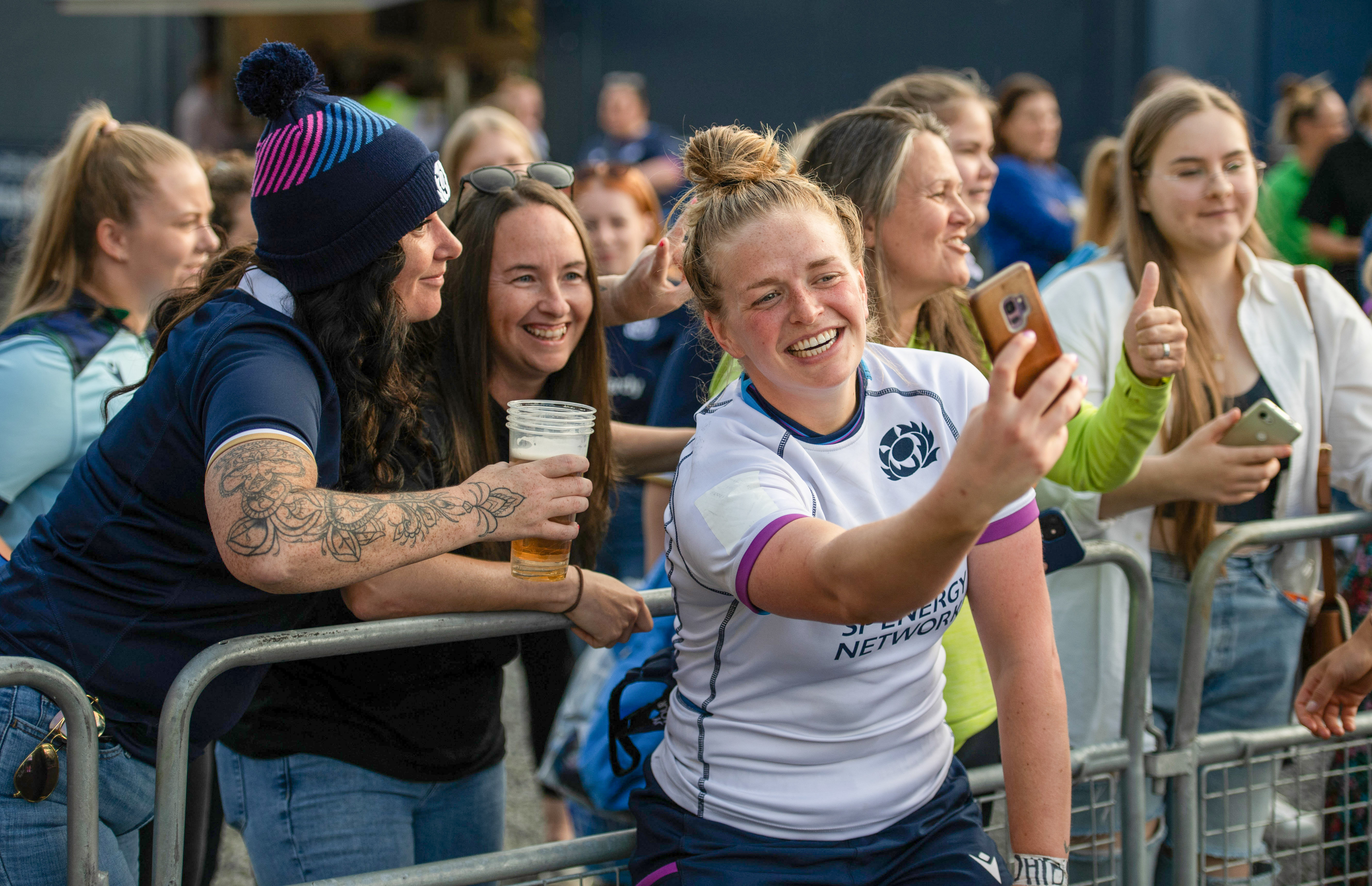 Image shows crowd behind metal gates as Rugby player takes a selfie with them.